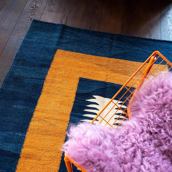 Nærbillede af et Gabbeh tæppe med geometrisk mønster i blå og gul, orange stol.